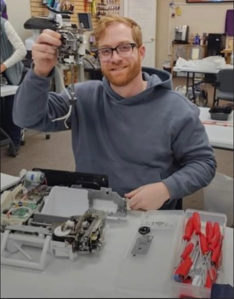 Blair, certified sewing machine technician, holding a part from a disassembled sewing machine at his repair bench in Trenton, Ontario